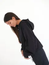 Buzo negro oversize de felpa con capucha y espalda descubierta, mangas largas, calce relajado y detalle de logo bordado en la parte inferior.