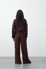 Pantalón de corte holgado y pierna ancha, con cintura elástica ajustable mediante cordón. Presenta bolsillos laterales y costuras verticales decorativas que recorren el frente de las piernas.