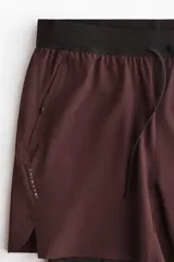 Short deportivo de doble capa en tejido funcional con tecnología DryMove para absorción de sudor. Presenta corte estándar, cintura elástica con cordón ajustable, bolsillos laterales y aberturas en el bajo. Incluye una capa interior tipo biker con bolsillo y bucle trasero para accesorios.