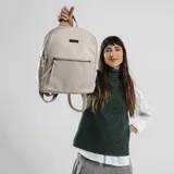 Mochila color beige con aplique de cuero sintético en la parte inferior y superior. Tiene un bolsillo frontal con cierre y un bolsillo interno. Las correas son regulables.