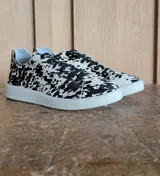 Zapatillas urbanas de cuero con pelo, estampado animal print tipo vaca en blanco y negro, con cordones negros y suela de goma blanca.