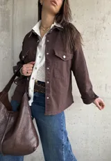 Sobrecamisa de gabardina color marrón chocolate, de corte holgado, con bolsillos con solapa en el pecho, mangas largas y cierre frontal de botones metálicos.