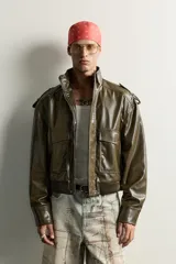 Cazadora cropped fit de color verde militar, confeccionada en tejido efecto piel. Presenta cuello subido, manga larga con puño abotonado, trabillas en los hombros, y bolsillos delanteros de plastrón con solapa. Su diseño incluye bajo elástico y cierre frontal con cremallera oculta por solapa con botones a presión.