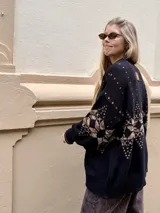 Saco de punto gris con diseño geométrico en color amarillo, cierre frontal con botones, cuello redondo y bordado de corazón pequeño en el pecho.