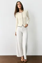 Chaqueta de punto marrón con cuello redondo, manga larga y ribetes en color rojo. Cuenta con cierre frontal de botones.