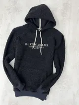 Canguro negro de tela corderito con capucha y cordones blancos. Estampado frontal con el texto "Duxon Jeans Los Angeles Est. 1982" en color blanco.