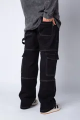 Pantalón tipo carpintero de corte relaxed fit y tiro medio, confeccionado en denim negro con costuras a contracolor en blanco. Presenta múltiples bolsillos cargo laterales, un bolsillo con cierre en la parte inferior y presillas utilitarias.
