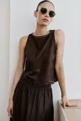 Top marrón oscuro de cuello redondo y manga sisa, con detalles de bordados y entredoses geométricos y florales a tono. Cuenta con abertura y cierre de botón en la espalda.