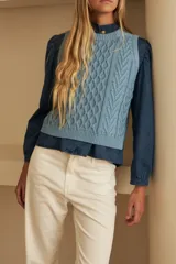 Chaleco de tejido de punto color marrón oscuro, con diseño de ochos y rombos en relieve. Tiene cuello redondo y es sin mangas.