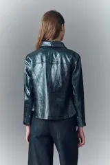 Camisa de cuero ovino verde metalizado, con cuello camisero y botones a presión con logo. Presenta un calce entallado.