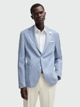 Blazer de hombre color azul claro con textura de tejido tipo lino o mezcla, de corte estructurado con solapas de muesca, dos botones frontales blancos y bolsillos de parche.