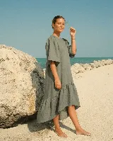 Vestido largo de lino color verde militar, de corte holgado, con mangas cortas abullonadas, cuello redondo y diseño asimétrico con volado en el ruedo, más largo en la parte trasera.
