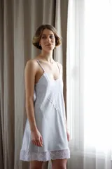 Camisón corto de satén color crema con detalles de puntilla gris en el escote y en el ruedo. Presenta breteles finos ajustables y un diseño fluido.