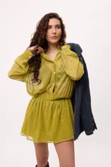 Vestido corto de chiffon color verde lima, con transparencia, cuello camisero, botones frontales y elástico en la cintura. Las mangas son largas y abullonadas con puños elásticos.