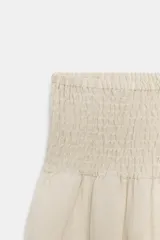 Pantalón ancho color beige claro, de tiro alto con cintura fruncida elástica. Las piernas son anchas y terminan en puños ajustables con cordones.