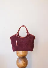 Cartera tipo tote de gamuza negra, con doble asa de mano y correa larga ajustable y desmontable. Cuenta con un diseño estructurado y base plana.