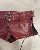 Short corto color bordó con efecto de cuero, tiro bajo, bolsillos frontales con cierre y detalle de hebilla con ojales metálicos.