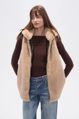 Chaleco sin mangas de pelo sintético color beige claro, con capucha y cierre frontal.