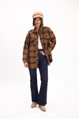Camisa de corte oversize con estampado de cuadros en tonos marrones y negros. Presenta cuello clásico, cierre frontal de botones metálicos y dos bolsillos con solapa en el pecho.