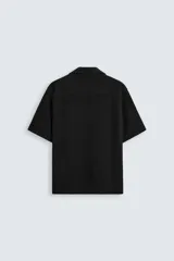 Camisa de corte regular fit confeccionada en tejido con estructura de color negro. Cuenta con cuello bowling, manga corta, aberturas laterales en el bajo y cierre frontal de botones.