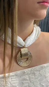 Choker compuesto por una cinta de encaje blanco y un dije circular grande de metal dorado con textura grabada.