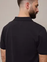 Remera polo negra de piqué de algodón con cuello clásico y tapeta de dos botones. Presenta un pequeño logo bordado en el pecho.