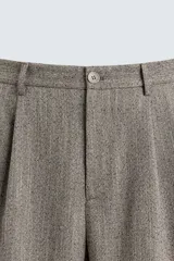 Pantalón relaxed fit color marrón con patrón de espiga, confeccionado en tejido con viscosa. Presenta pliegues frontales, bolsillos laterales y bolsillos traseros de vivo. Cierre frontal con cremallera y botón.