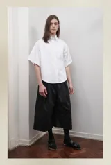 Bermuda negra unisex de corte sastrero, con pretina elástica, tiro bajo, bolsillos laterales y cierre lateral. Presenta un pliegue delantero de gran tamaño.