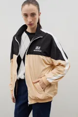 Campera de tela avión con diseño color block en negro y verde, con detalles de franjas blancas en las mangas. Presenta cierre frontal completo, cuello alto, puños y ruedo elásticos, y logo bordado en el pecho.