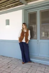 Chaleco de cuero gamuzado color marrón, con cierre frontal mediante dos hebillas metálicas y dos bolsillos frontales con solapa.