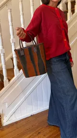 Matera de cuero con diseño de paneles verticales en combinación de colores azul, verde, marrón y bordó. Cuenta con dos asas cortas de cuero y estructura rígida.