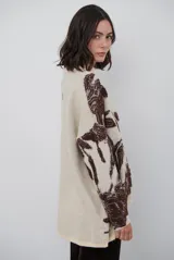 Buzo de tejido de punto con diseño floral en contraste, cuello redondo y mangas largas. Presenta una textura suave y un corte holgado.