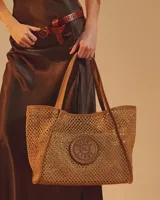 Cartera tipo tote de diseño tejido tipo red color tostado, con asas y detalles en cuero sintético del mismo tono. Incluye un aplique circular frontal perforado con el logo de la marca.