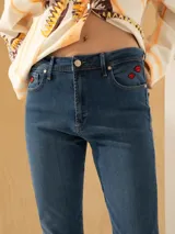 Jeans slim de tiro medio color azul, con largo al tobillo y parches bordados de labios rojos en el bolsillo delantero.