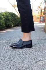 Zapato de cuero negro con puntera charolada, laterales texturados y pequeño taco cuadrado.