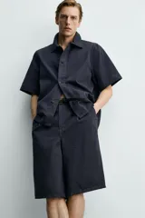 Bermuda de corte relajado confeccionada en denim de algodón rígido, con pliegues frontales, bolsillos laterales y bolsillos traseros de vivo. Cuenta con cierre frontal de cremallera y botón.
