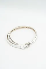 Cinturón fino de color blanco con ojales metálicos a lo largo de toda la tira y hebilla plateada.