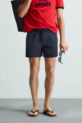 Bañador de hombre color azul marino, confeccionado en tejido técnico, con cintura elástica ajustable mediante cordón. Presenta bolsillos laterales y un bolsillo trasero de plastrón. Incluye forro interior.