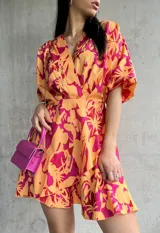 Vestido corto color naranja con estampado floral fucsia, escote cruzado, mangas cortas abullonadas y falda con volados.