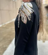 Buzo color crudo de mangas largas con apliques de lentejuelas plateadas y doradas en los hombros.