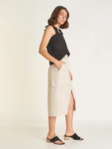 Falda midi color beige, de tiro alto con elástico en la cintura trasera, cierre y botón delantero. Tiene bolsillos delanteros y bolsillos cargo a los costados, con tajo en el delantero.