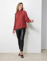 Blusa color ladrillo de gasa plisada con cuello alto, manga larga abullonada con puño y botón de ajuste. Espalda con abertura ojal y doble abotonadura.