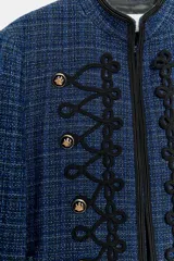Blazer corto de tweed en color azul, con cuello mao y manga larga. Presenta detalles de pasamanería negra en el frente y cierre con ganchos metálicos y falsos botones dorados.