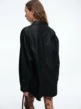 Chaqueta camisera de corte oversize en color negro, confeccionada en cuero sintético. Presenta cuello clásico, cierre frontal con botones y mangas largas con puños abotonados.