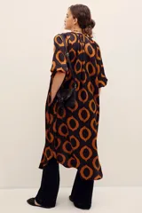 Vestido midi de viscosa color negro con estampado geométrico de círculos en tonos marrones y naranjas, de manga corta y corte recto con aberturas laterales.