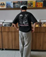 Remera oversize negra con diseño gráfico en la espalda que incluye la inscripción "Kaboa Radio" y un personaje ilustrado, de corte amplio y mangas cortas.