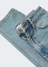 Pantalón de jean celeste de tiro alto, corte mom fit y largo al tobillo. Confeccionado en tejido de algodón estilo tejano vaquero, con trabillas, cinco bolsillos y cierre de cremallera y botón.