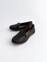 Mocasines de cuero color dorado con acabado texturizado, diseño clásico de punta redondeada y costuras visibles en el empeine. Cuentan con suela plana y flexible.