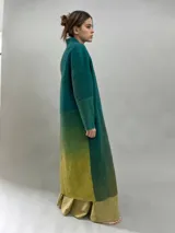 Tapado largo de lana merino afieltrada con diseño de paneles en degradé de tonos verdes y ocres. Presenta hombros caídos, mangas rectas, bolsillos laterales y cierre frontal con broches ocultos.