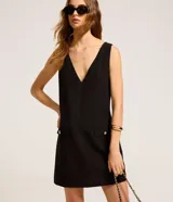 Vestido corto negro de crepé con escote en V tanto en la parte delantera como en la trasera. Tiene bolsillos delanteros con botones dorados.